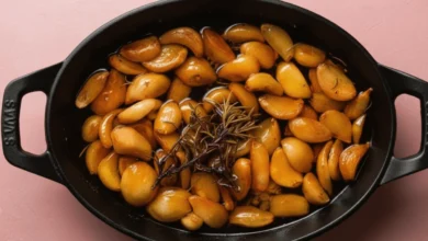 Garlic confit cooking with rosemary in a skillet.