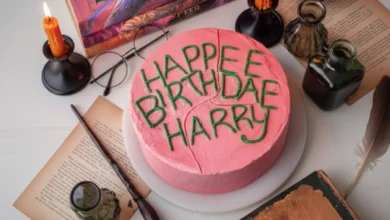 A whimsical "Cake of Harry Potter" decorated with pink frosting and green icing reading "HAPPEE BIRTHDAE HARRY," surrounded by magical props like candles and potions.