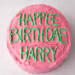 A whimsical "Cake of Harry Potter" decorated with pink frosting and green icing reading "HAPPEE BIRTHDAE HARRY" in a playful, misspelled design
