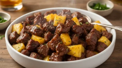 Sticky pineapple steak bites with tender beef cubes and fresh pineapple pieces, garnished with herbs in a white bowl.