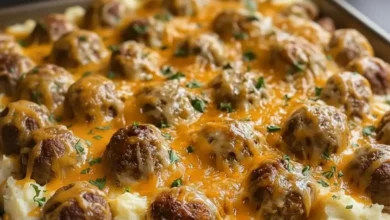Meatballs and mashed potatoes topped with melted cheese and fresh herbs, served in a hearty, comforting dish.