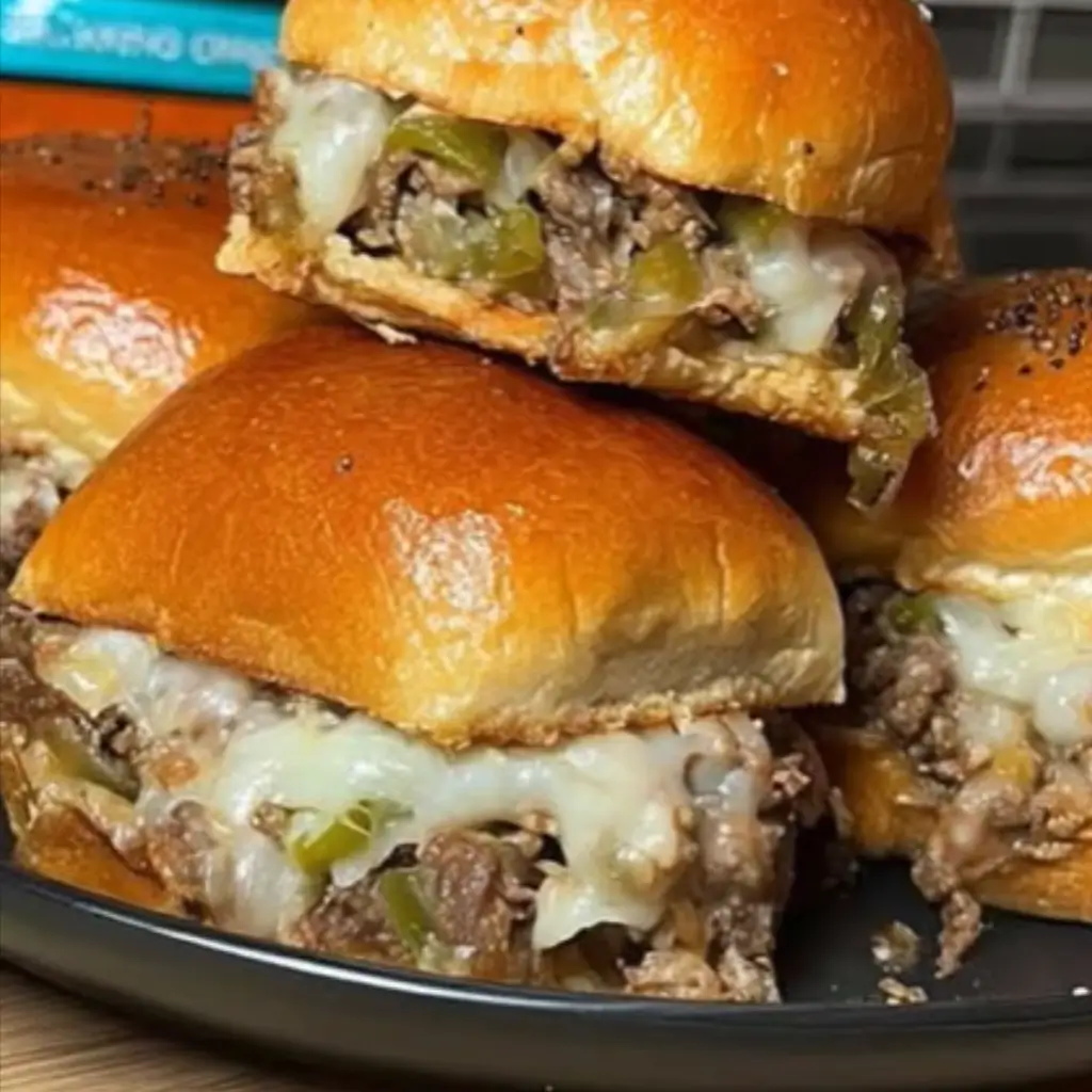 Close-up of Philly Cheesesteak Sliders with melted cheese, seasoned beef, and green peppers spilling from soft slider buns on a plate.