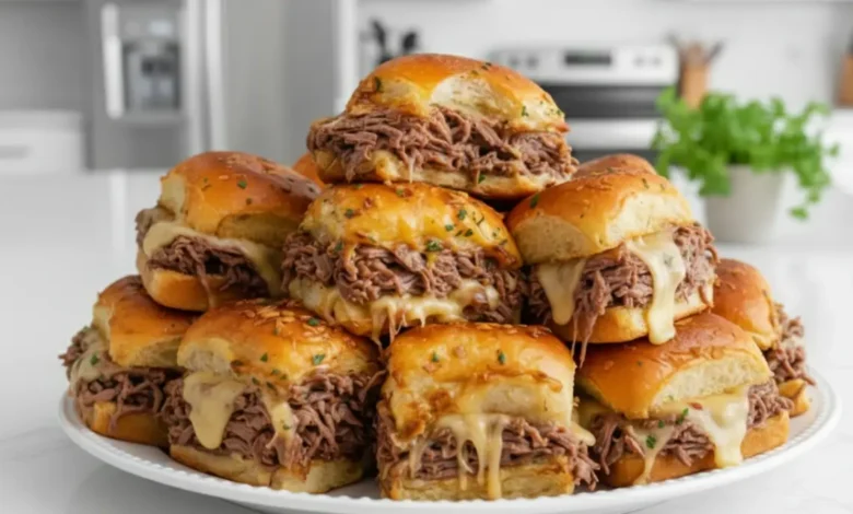 A plate of freshly made French Dip Sliders stacked high, with tender roast beef, melted cheese, and golden, soft slider buns topped with herbs.