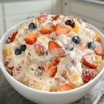 A close-up of a bowl of Cheesecake Fruit Salad, filled with fresh strawberries, blueberries, and pineapple chunks in a creamy dressing.