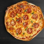 A freshly baked sourdough pizza with pepperoni slices, melted cheese, and basil leaves on a rustic wooden table, showcasing a golden and crispy crust.