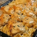 Close-up of chicken noodle casserole with golden-brown chicken pieces, creamy sauce, and pasta topped with herbs and cheese.