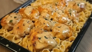Close-up of chicken noodle casserole with golden-brown chicken pieces, creamy sauce, and pasta topped with herbs and cheese.