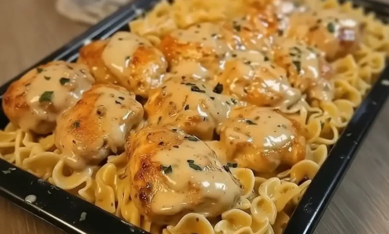 Close-up of chicken noodle casserole with golden-brown chicken pieces, creamy sauce, and pasta topped with herbs and cheese.