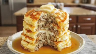 Stack of pancakes filled with sausage, topped with butter and drenched in syrup.