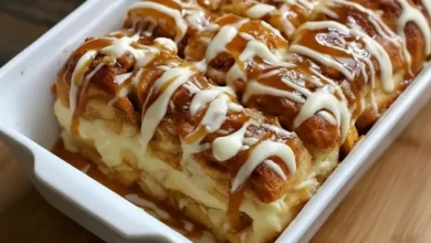 Freshly baked cinnamon roll apple lasagna layered with creamy filling, apple pie center, caramel drizzle, and vanilla icing in a white baking dish.