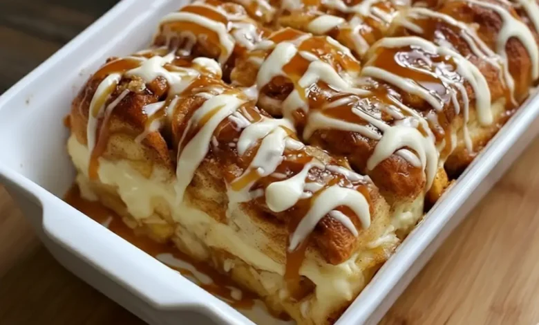Freshly baked cinnamon roll apple lasagna layered with creamy filling, apple pie center, caramel drizzle, and vanilla icing in a white baking dish.