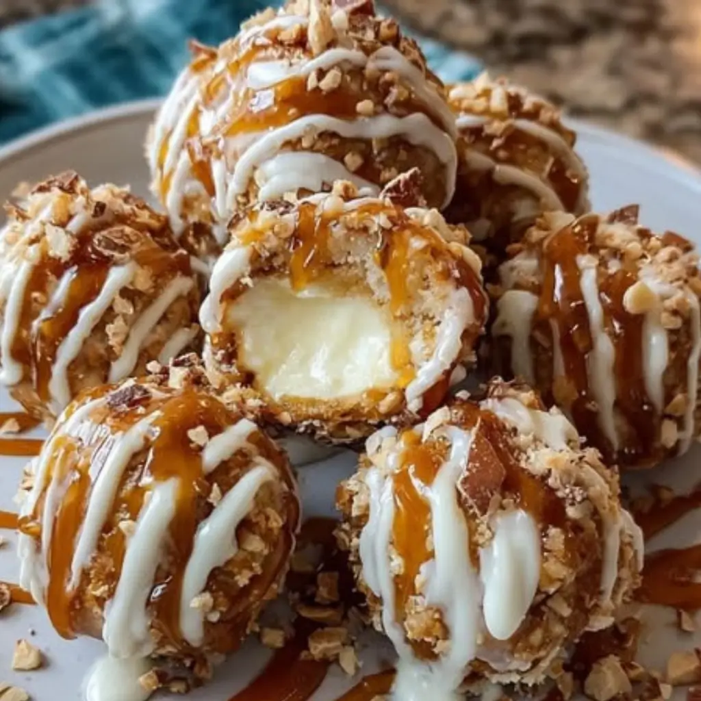 Salted caramel pretzel cheesecake balls coated in crushed pretzels and nuts, drizzled with caramel and white chocolate, with one cut open revealing creamy cheesecake center.