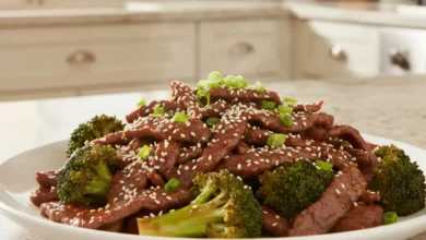 Beef and broccoli stir-fry with sesame seeds and green onions on a white plate.