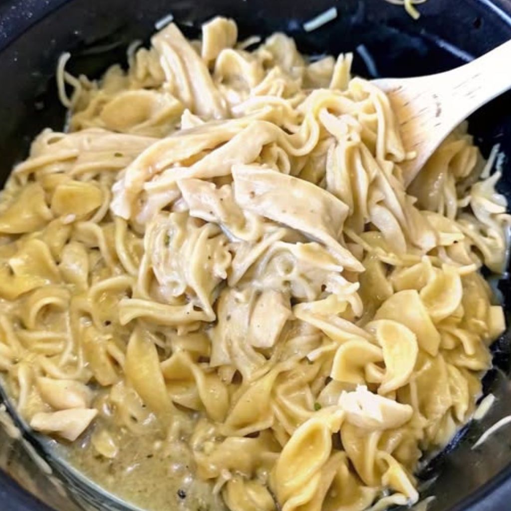 A close-up view of Crockpot Chicken and Noodles, featuring tender shredded chicken and egg noodles, topped with fresh parsley and black pepper.