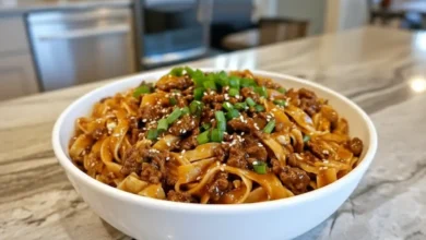 Bowl of Mongolian noodles with ground beef, garnished with green onions and sesame seeds, served on a kitchen countertop.