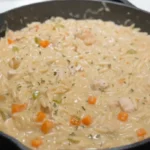 Close-up of creamy chicken pot pie orzo with tender chicken, carrots, and vegetables in a skillet on the stove.