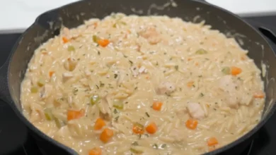 Close-up of creamy chicken pot pie orzo with tender chicken, carrots, and vegetables in a skillet on the stove.