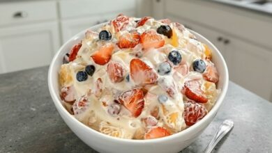 A close-up of a bowl of Cheesecake Fruit Salad, filled with fresh strawberries, blueberries, and pineapple chunks in a creamy dressing.