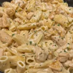 Creamy parmesan garlic chicken pasta with rigatoni and chicken pieces in a skillet, topped with parsley