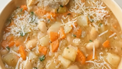 Close-up of slow cooker white bean soup with carrots, potatoes, grated Parmesan cheese, and a slice of crusty bread on top.