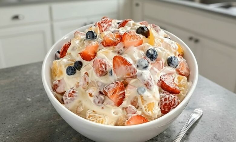 A close-up of a bowl of Cheesecake Fruit Salad, filled with fresh strawberries, blueberries, and pineapple chunks in a creamy dressing.