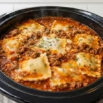 Delicious Crockpot Ravioli Lasagna with melted cheese and ground beef, cooking in a slow cooker.